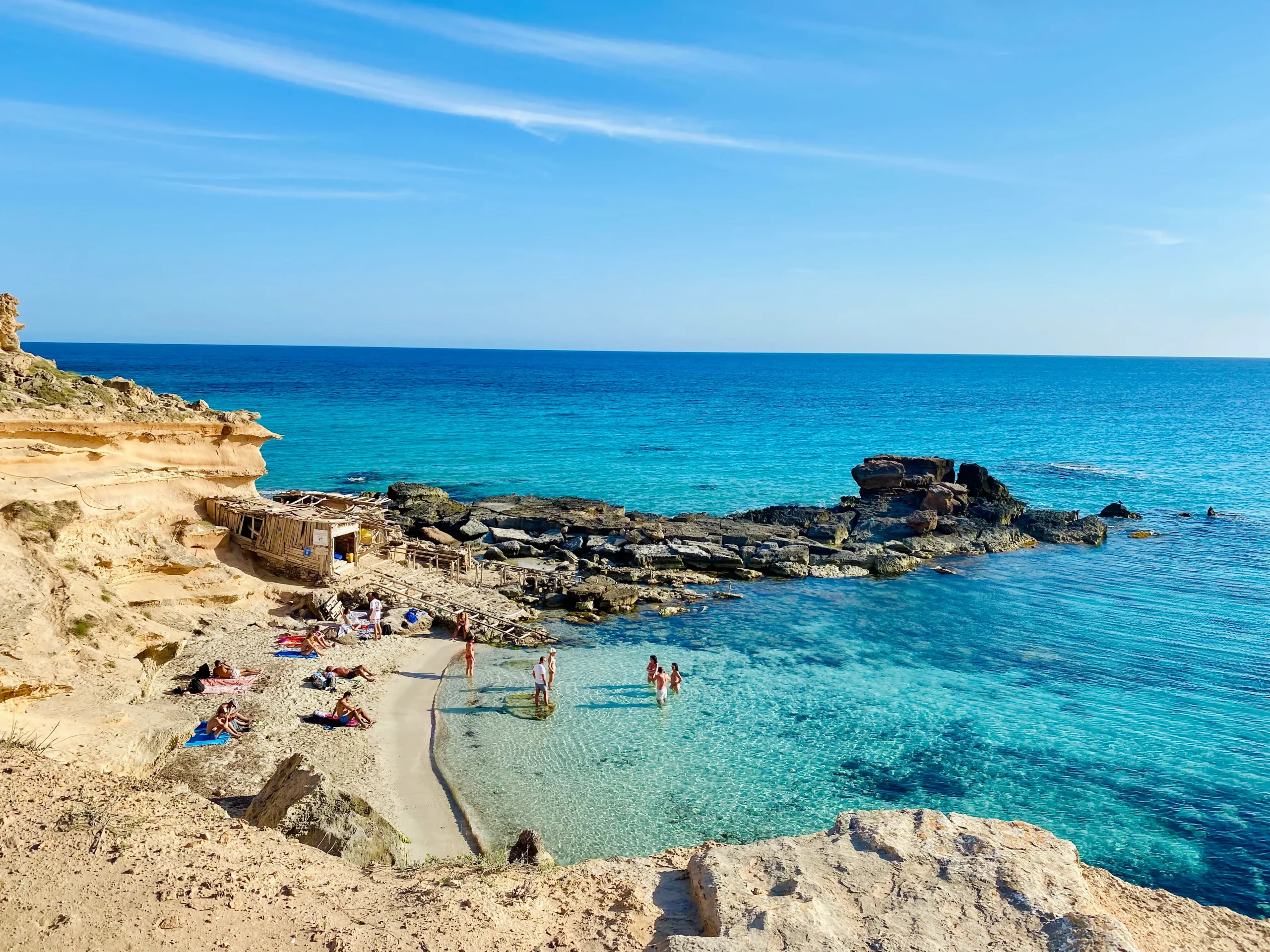 Caló des Mort, hidden cove in Formentera with reddish rocks and turquoise water under clear skies.